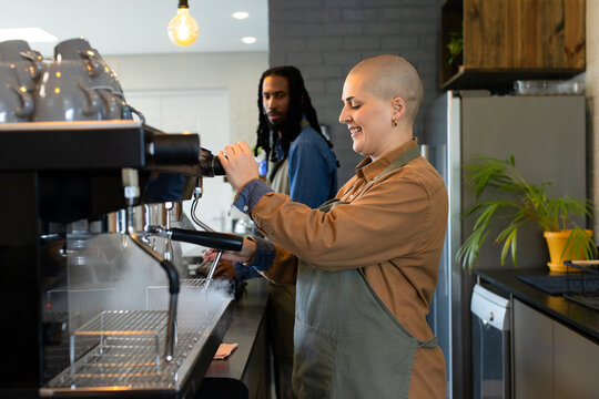Diverse barista coworkers operating espresso machine behind coffee shop counter using steam wand
