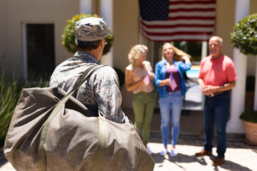 Obraz premium Caucasian military soldier with bag walking towards family standing at the entrance