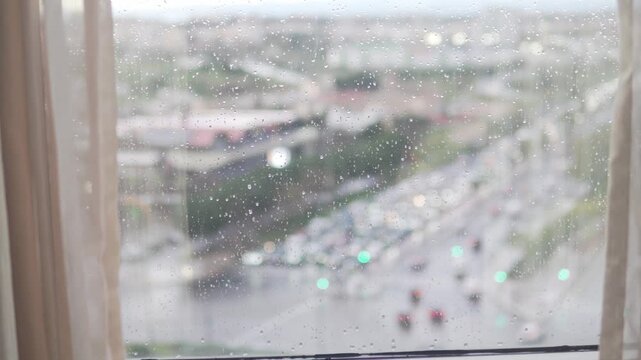 Rainy city traffic seen through a home window covered with raindrops. Cars moving along a busy road on a wet day, soft focus urban background with calm, moody atmosphere and everyday lifestyle