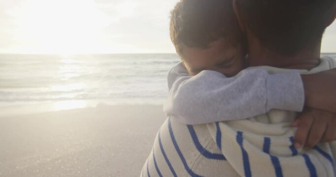 Portrait of hispanic father embracing son on beach at sunset