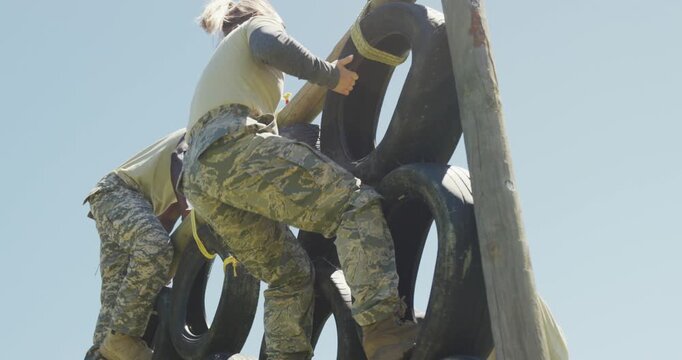 Diverse group male soldier in combat uniform climbing tyre wall on army obstacle course in the sun