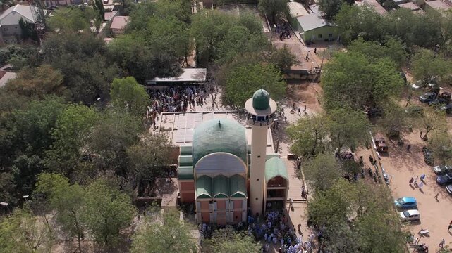 Aerial view of a mosque with green dome amid trees and buildings, people gathering around the mosque, Kano, Kano, Nigeria.