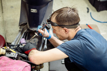 Mechanic Soldering Wires During Scooter Repair in Workshop