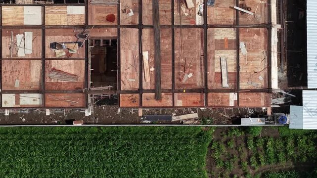 Aerial view of a building under construction contrasting with the lush green fields, Klaten Regency, Central Java, Indonesia.