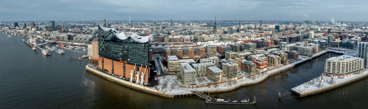 Wide aerial panorama of Hamburg&rsquo;s HafenCity in winter with iconic concert hall, modern waterfront architecture, canals, marinas and snow-covered rooftops along the Elbe River.