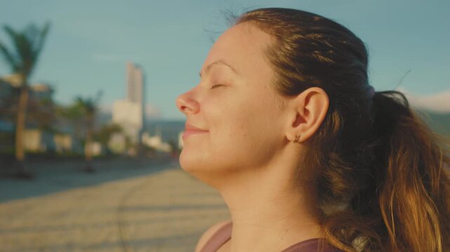 Woman standing in profile with closed eyes, meditating and taking a deep breath on a sandy beach during a beautiful golden hour sunrise, finding peace