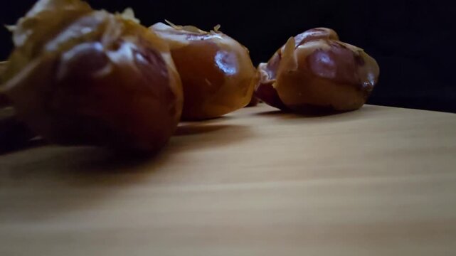 A high-quality, close-up shot of premium Saudi Khalas dates with a glossy golden-brown texture and thin skin, elegantly arranged on a rustic wooden board against a moody dark background, highlighting 