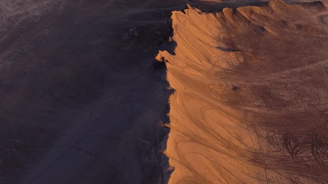 Aerial view of a desolate desert landscape at dusk, the warm light accentuating tyre tracks in the sand, Hanksville, Utah, United States.