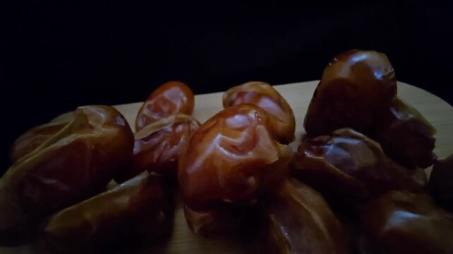 A high-quality, close-up shot of premium Saudi Khalas dates with a glossy golden-brown texture and thin skin, elegantly arranged on a rustic wooden board against a moody dark background, highlighting 