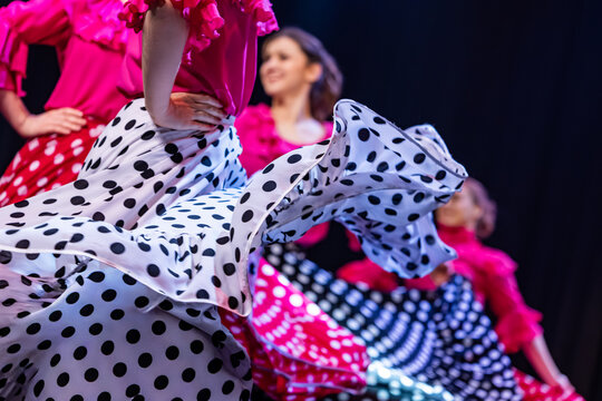 Close-up of flamenco dancers in vibrant polka-dot skirts and ruffled pink tops performing with swirling motion on stage, capturing cultural flair and rhythm