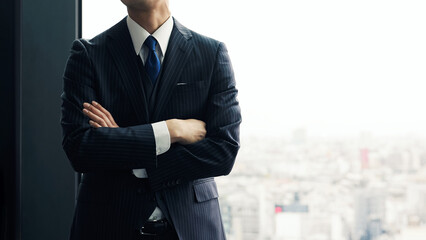 オフィスで都市を背景に腕組みする男性ビジネスパーソン