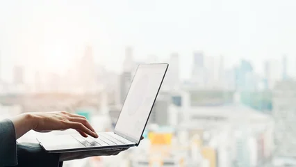Fotobehang Restaurant Woman using a laptop with a city in the background  © metamorworks