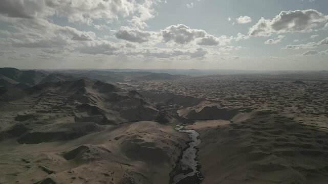 Aerial view of drone descending over unique desert river in Mongolia, wide shallow water emerging from sand dunes, popular tourist landmark, wilderness landscape, 4k raw unedited footage
