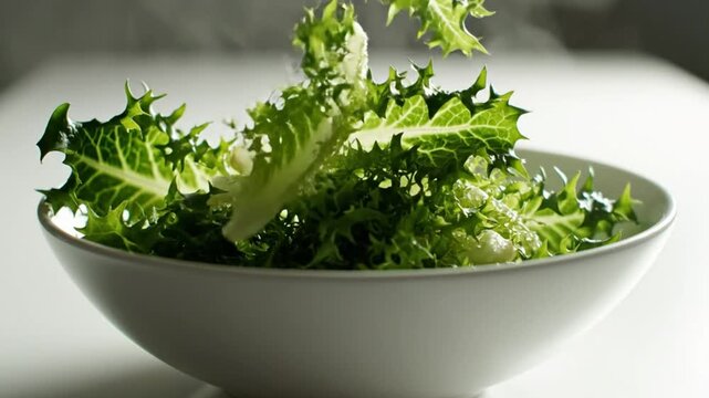 Fresh frisee lettuce being gently placed into a clean white bowl for a healthy salad preparation
