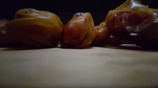 A high-quality, close-up shot of premium Saudi Khalas dates with a glossy golden-brown texture and thin skin, elegantly arranged on a rustic wooden board against a moody dark background, highlighting 