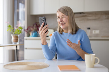 Happy senior woman using a smartphone for a video call, communicating with loved ones remotely from...