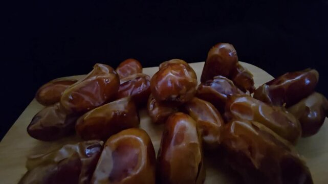 A high-quality, close-up shot of premium Saudi Khalas dates with a glossy golden-brown texture and thin skin, elegantly arranged on a rustic wooden board against a moody dark background, highlighting 
