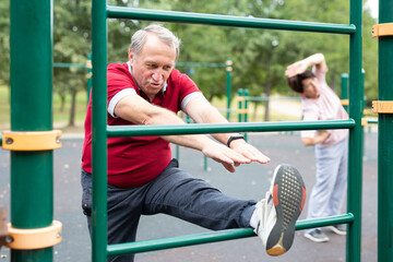 Obraz premium elderly man stretches on horizontal bars in an outdoor sports area