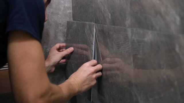 A man glues wall panels onto old tiles. A quick and affordable renovation