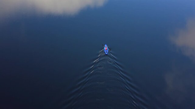 Aerial view of a lone kayaker cutting through the calm, dark blue waters of Loch Lubnaig reflecting the sky, Callander, Scotland, United Kingdom.