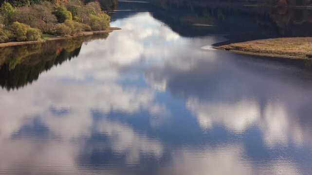 Aerial view of a lone kayaker cutting through the still, reflective waters mirroring the sky, surrounded by trees, Kielder, Northumberland, United Kingdom.