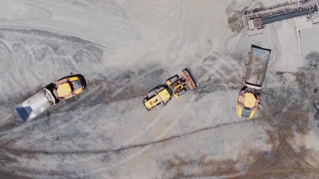 Aerial view of heavy machinery contrasting against the grey quarry floor, creating a stark industrial landscape, Blouberg, South Africa.