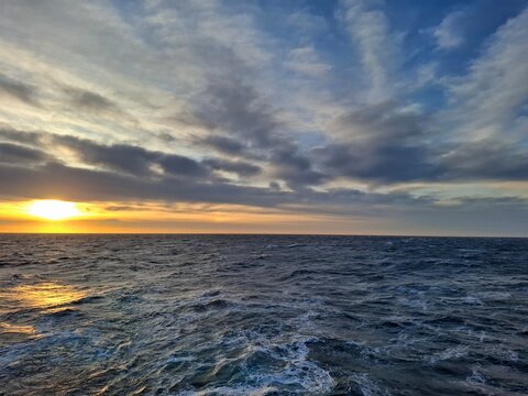 Golden sunset over cold open ocean with textured waves and layered clouds. Scenic seascape and travel inspiration background.