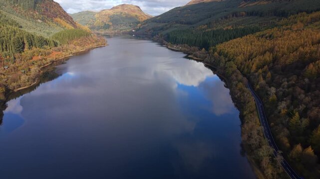 Aerial view of Loch Lubnaig's tranquil waters mirroring the sky, bordered by vibrant forests in autumn hues, Callander, Scotland, United Kingdom.