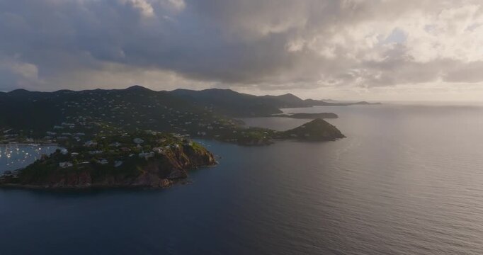 Aerial view of dramatic cliffs meet the vast ocean, with buildings nestled amongst the green hillsides, St John, US Virgin Islands.