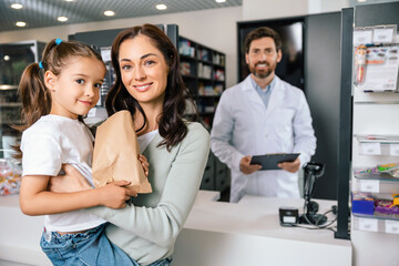 Fototapeta premium Happy mother holding daughter and paper bag receiving professional advice