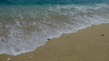 Waves on the beach. Gentle sea waves wash over a sandy beach shoreline. Clear ocean water and white foam meet smooth coastal sand.