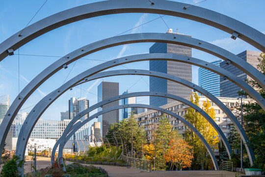 Arches frame a park walkway with an urban skyline in daylight autumn in Promenade de la Rose de Cherbourg Paris La Defense modern