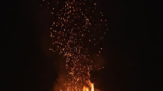 Dramatic orange hot sparks ascending high from intense flames in absolute darkness at night.