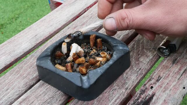 Close up hand extinguishing cigarette in dirty old ashtray. . Concept of unhealthy habits, addiction and everyday reality, routine and consequences of smoking