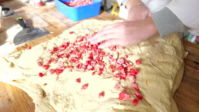 Baker sprinkles pink pralines by hand onto rolled pastry dough