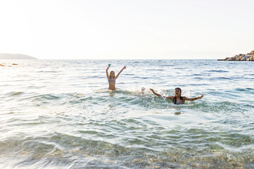 Happy children playing in shallow water of beach with arms raised and splashing
