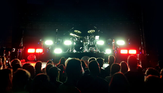 Crowd gathers for a live music performance in a venue with bright lights and a drum set on stage