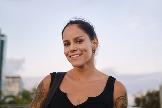 Latina woman smiling, showing piercing and arm tattoo
