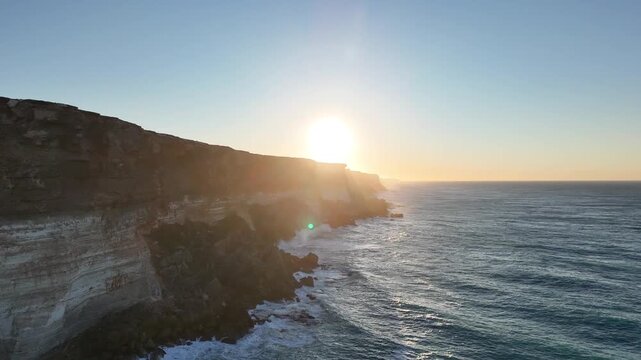 Aerial drone flight tracing the Bunda Cliffs over the ocean toward the bright morning sun in South Australia
