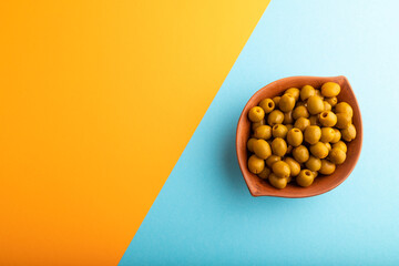 Fresh green olives in ceramic clay bowl on blue and orange pastel paper. Top view, flat lay