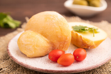 Smoked Mozzarella cheese, with tomatoes and olives on brown wooden, linen textile, side view, close up, selective focus.