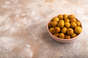 Ripe Longan in ceramic bowl on brown concrete, side view, copy space