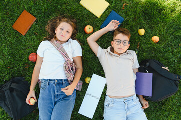 Naklejka premium Schoolchildren relaxing on grass with books and apples