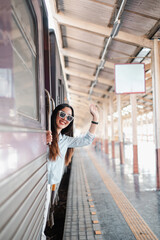 Obraz premium Cheerful woman waving from train window at station, capturing the joy of travel and adventure.