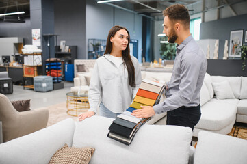 Woman consulting salesperson choosing fabric samples in furniture store