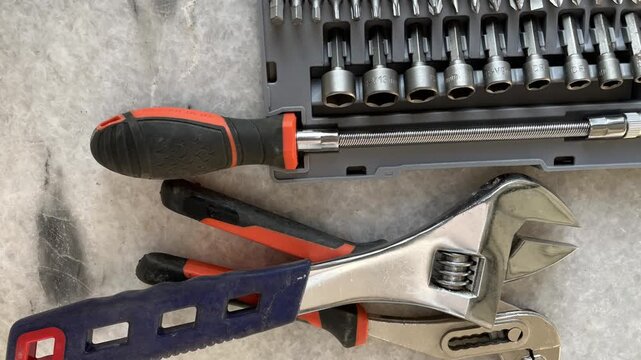 Adjustable wrench, plier, and screwdriver bit set on a stone surface