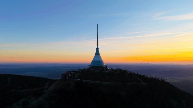 Watch the sunset from Jested Mountain in Czechia. The scene shows the Jested transmitter and hotel with golden light over the landscape. This place offers amazing views of the area.