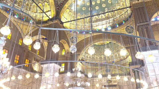 Interior view of the ornate ceiling and hanging lamps inside the Mosque of Ali in Cairo, Egypt. Detailed Islamic architecture with decorative patterns and historic design.