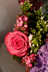 Vertical close-up of a pink rose with water droplets in a bouquet with pink hypericum berries and purple hydrangea.