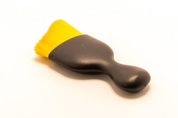 Obraz premium A small, black-handled brush with bright yellow bristles rests on a clean white surface. This tool is commonly used for dusting delicate electronics or small surfaces.
